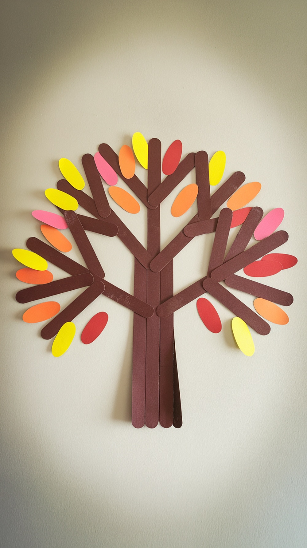 A crafted autumn tree made from popsicle sticks and colorful paper leaves.