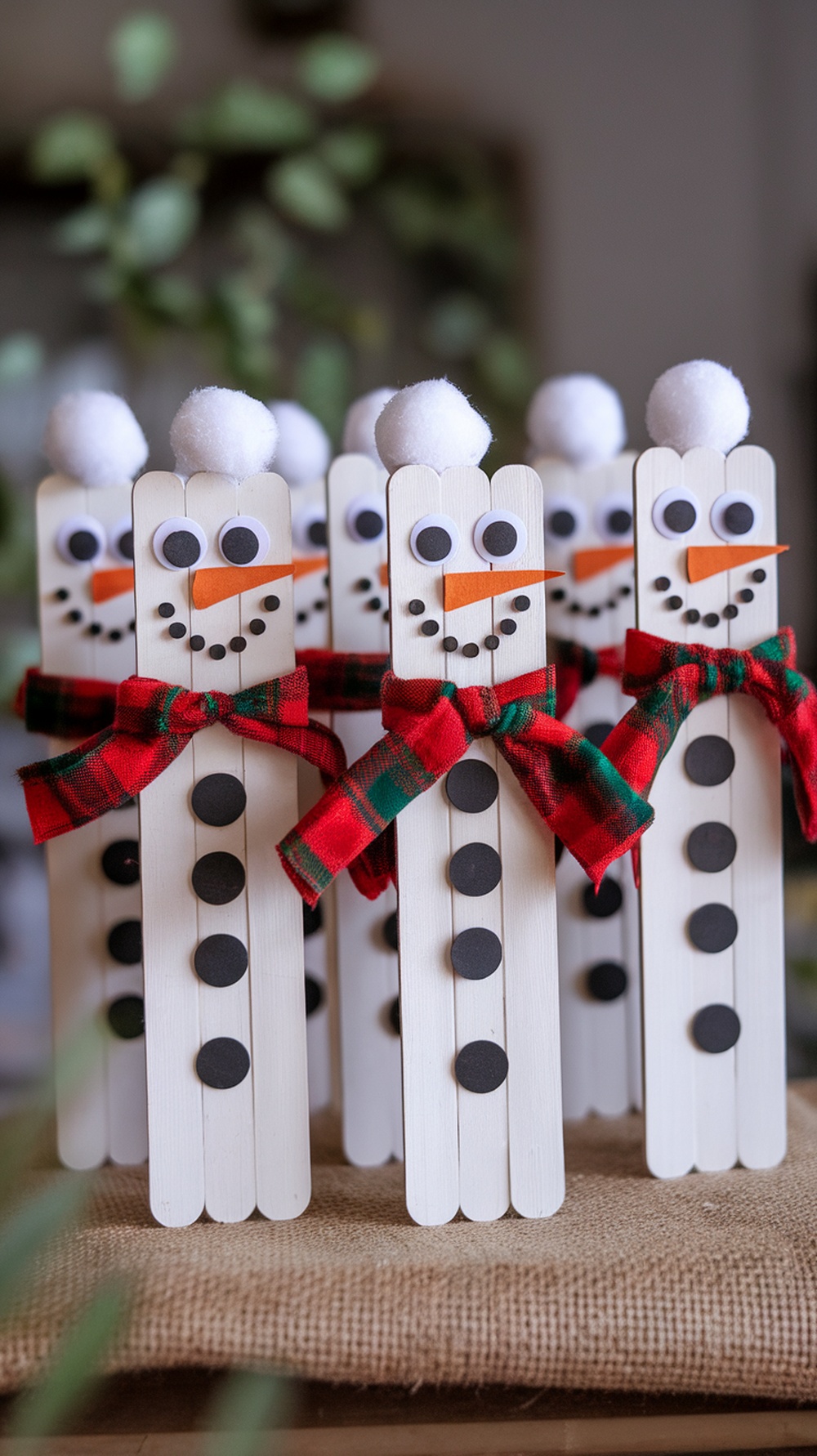 A group of popsicle stick snowmen with googly eyes, orange noses, and plaid scarves.
