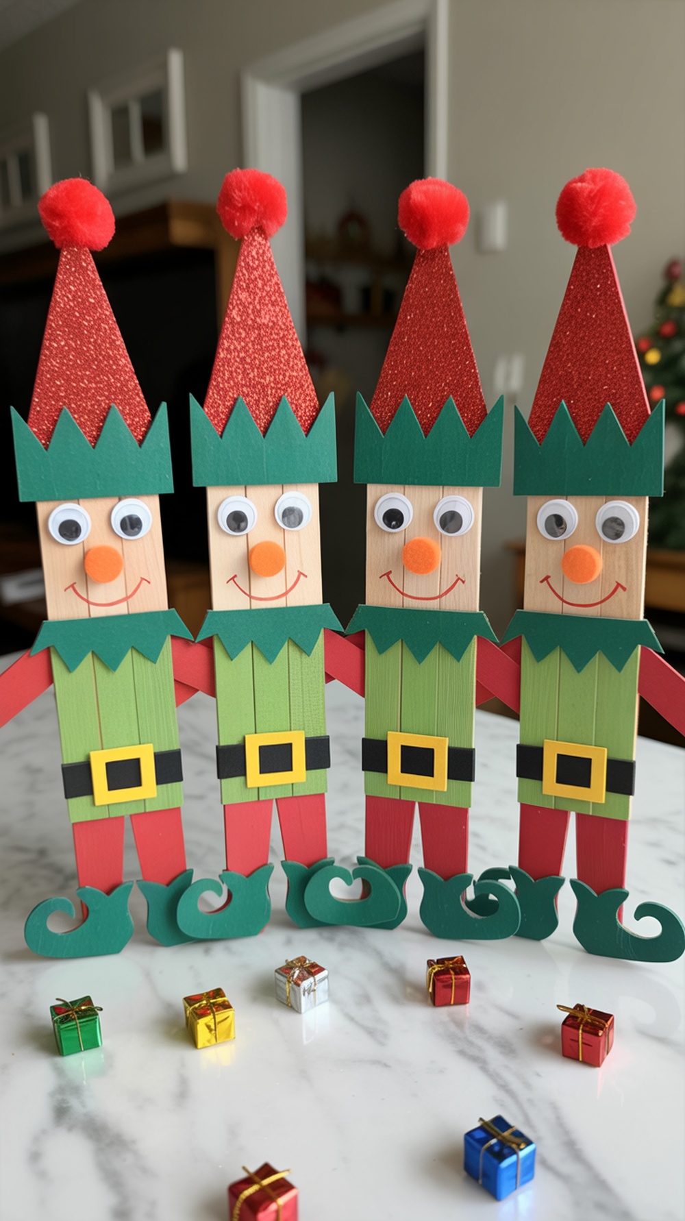 Four colorful Popsicle stick Christmas elves on a marble table surrounded by tiny wrapped gifts.