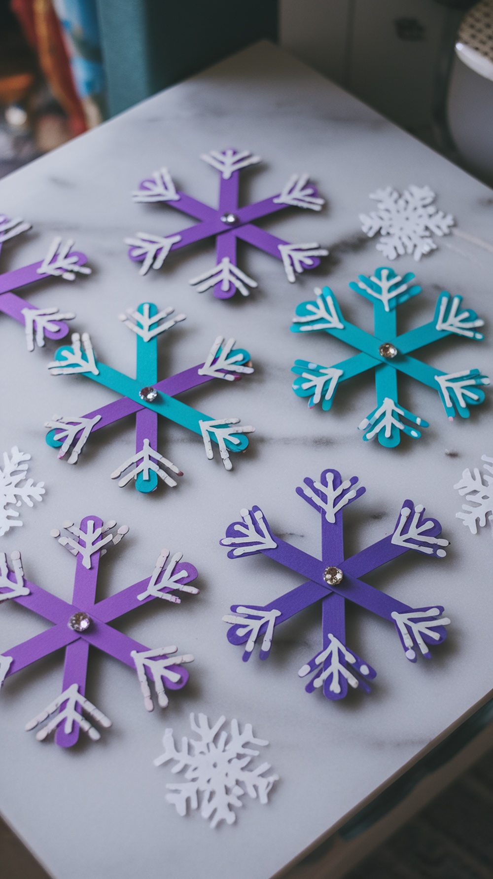 Colorful popsicle stick snowflakes spread out on a surface.