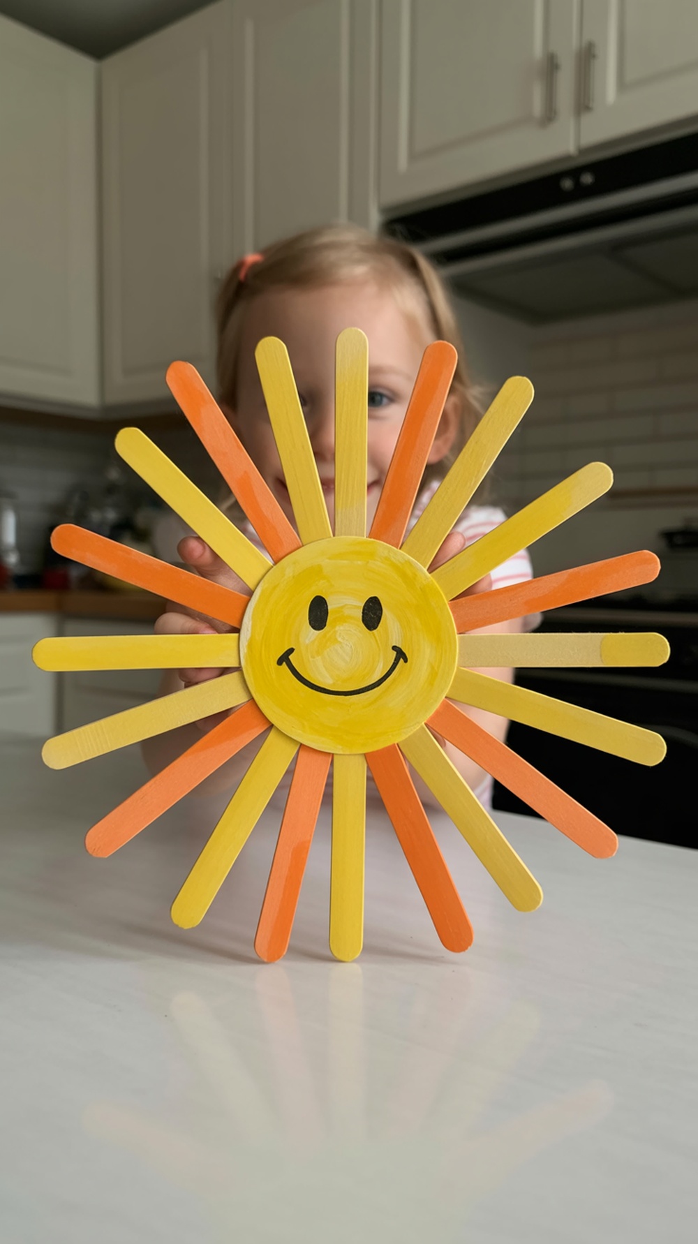 Popsicle stick sunshine wall art with a smiling face in the center, created from colorful popsicle sticks.