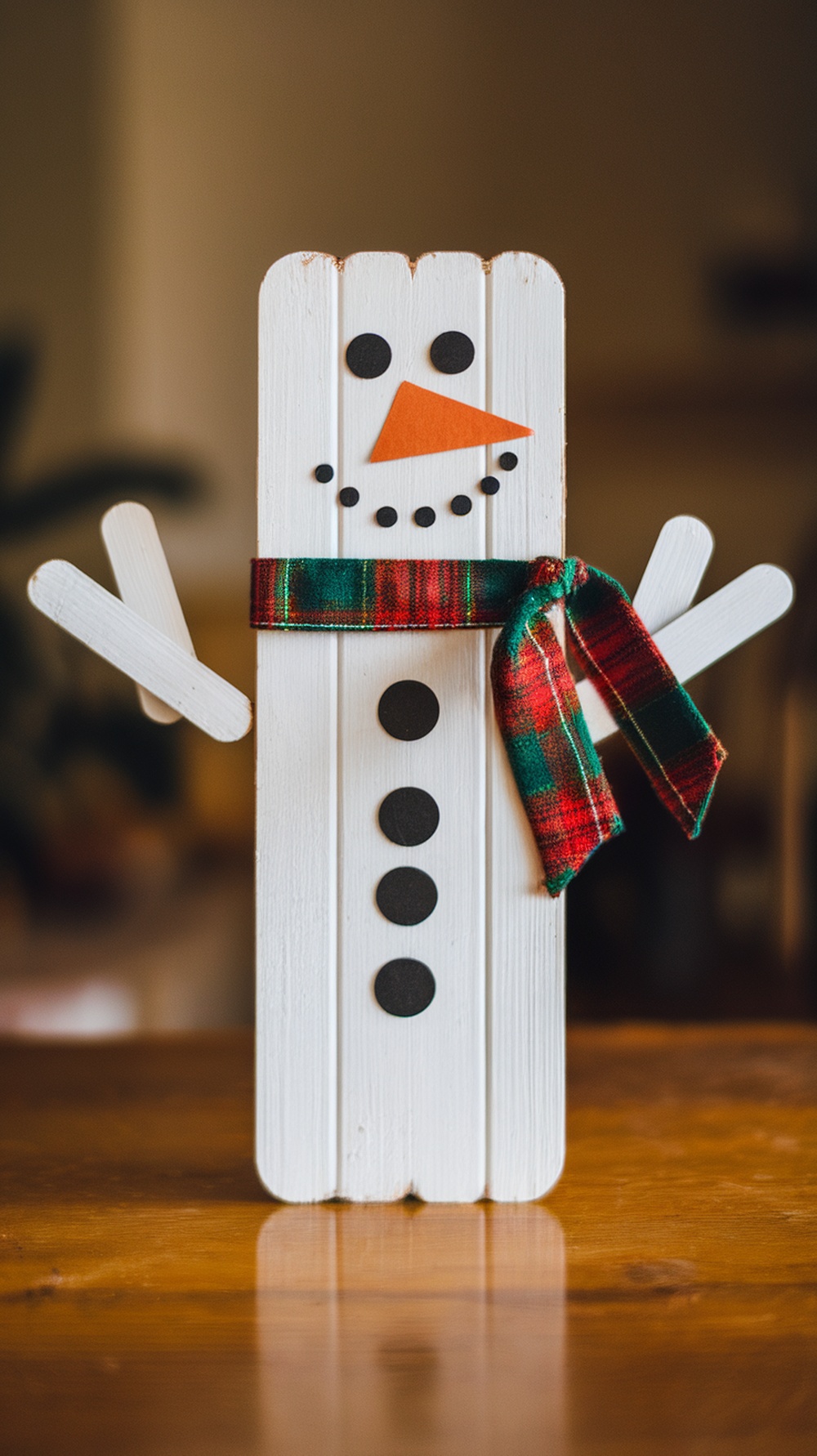 A cheerful popsicle stick snowman, decorated with a scarf, buttons, and stick arms.