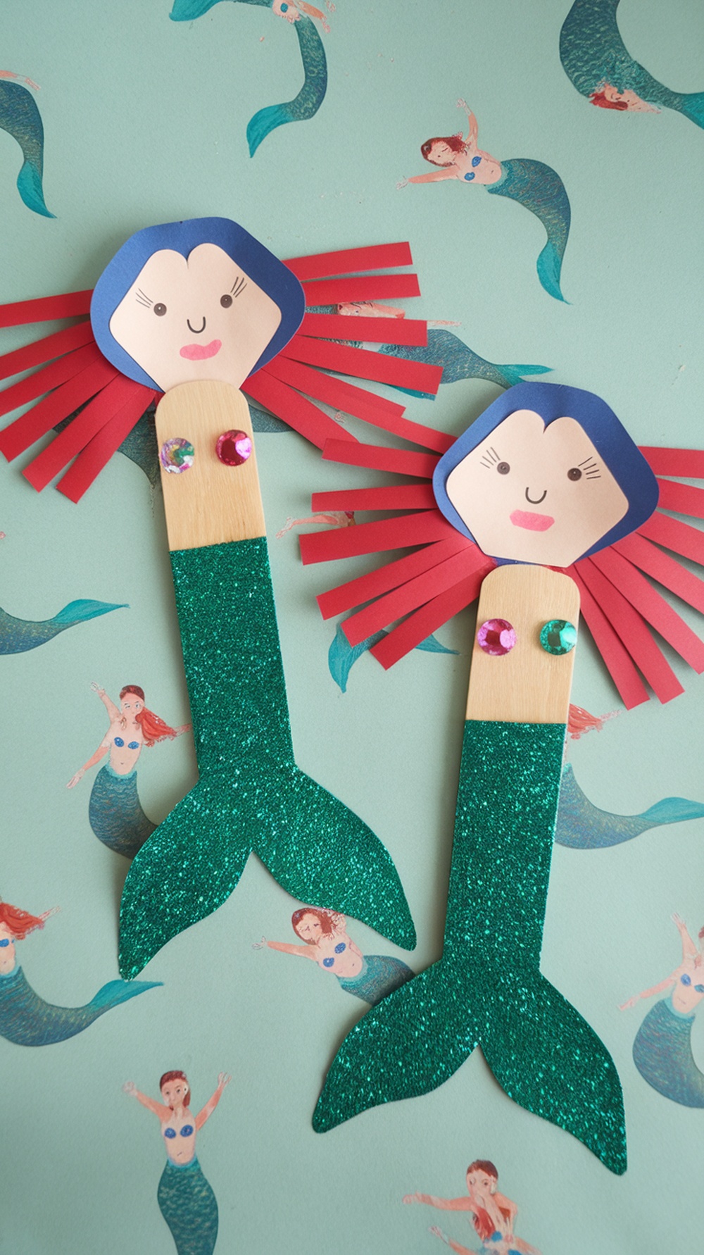 Two colorful popsicle stick mermaid puppets with glittery tails and hair made of paper strips.