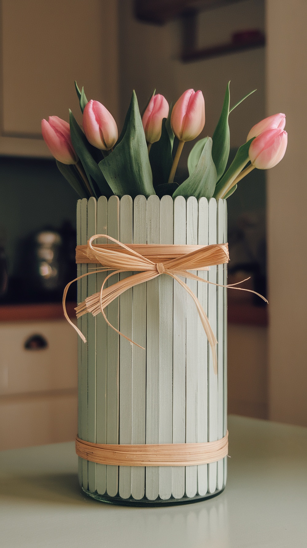 A handmade vase made from popsicle sticks holding pink tulips, tied with a ribbon.